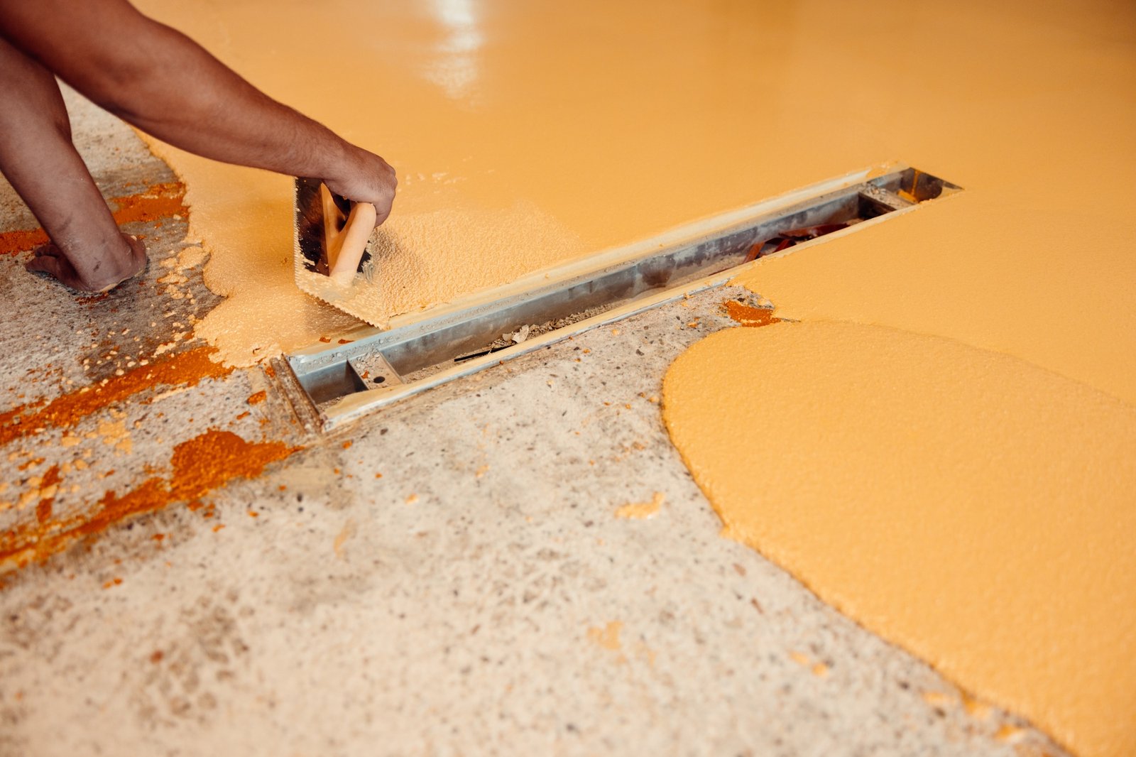 Construction worker applying epoxy resin with trowel to even concrete floor